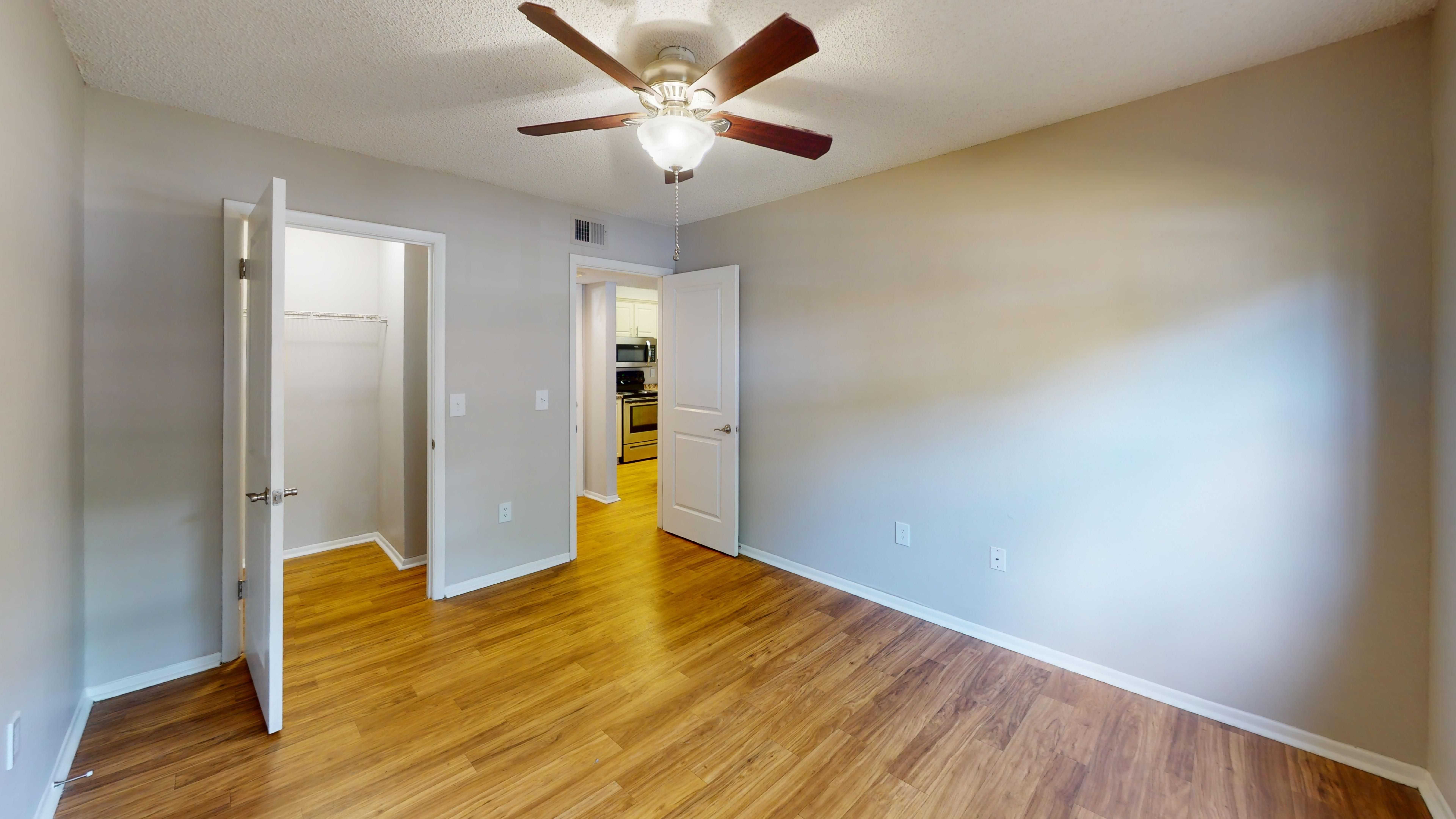 Retreat to a spacious bedroom in The Oakwood floor plan at Carrington Lane featuring wood-style flooring, a ceiling fan, and a walk-in closet.