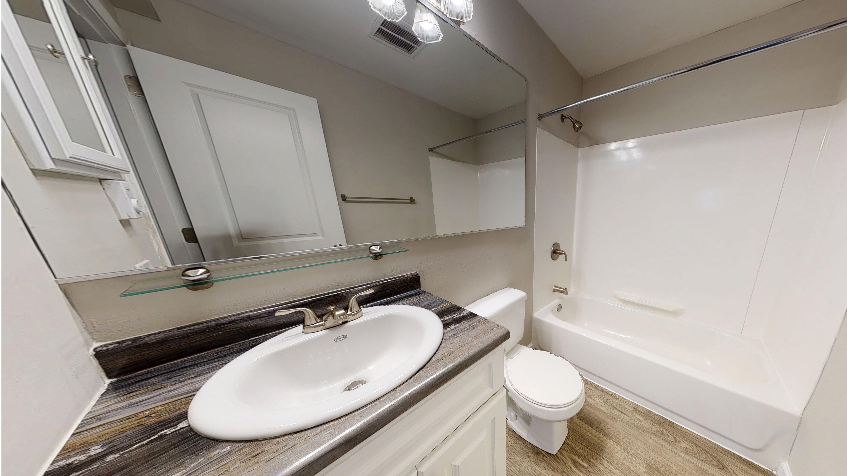 The bathroom in our Hampshire studio floor plan features a large mirror, wood-style flooring, and upgraded countertops.