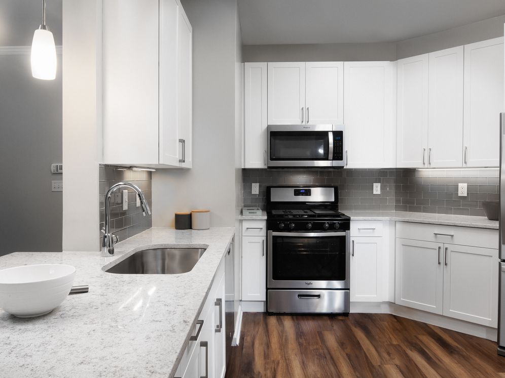 Classic Finish kitchen with white cabinetry, white quartz countertops, tile backsplash, stainless steel appliances, and hard surface flooring