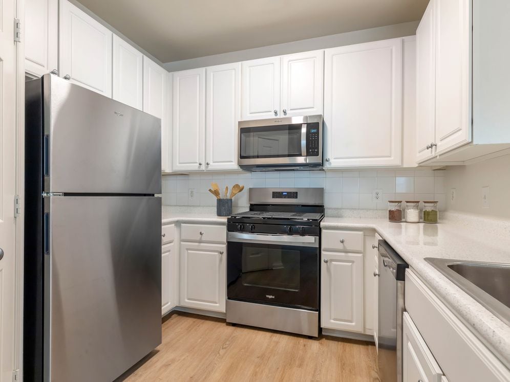 Classic I kitchen with white cabinetry, white laminate countertops, white tile backsplash, stainless steel appliances, and hard surface flooring