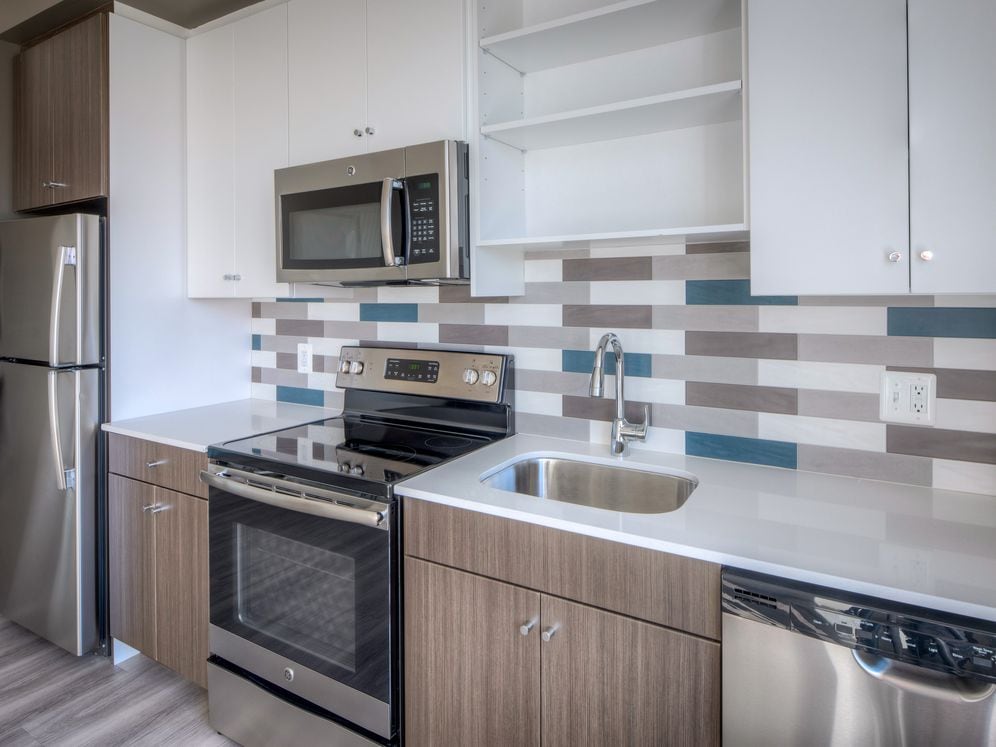 Kitchen with two tone cabinetry, quartz countertop, stainless steel appliances, tile backplash and hard surface flooring