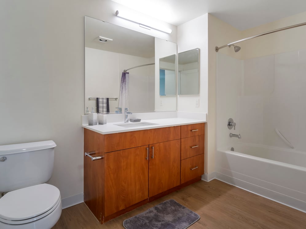 Renovated Package I bath with white quartz countertops, cherry cabinetry, and hard surface flooring