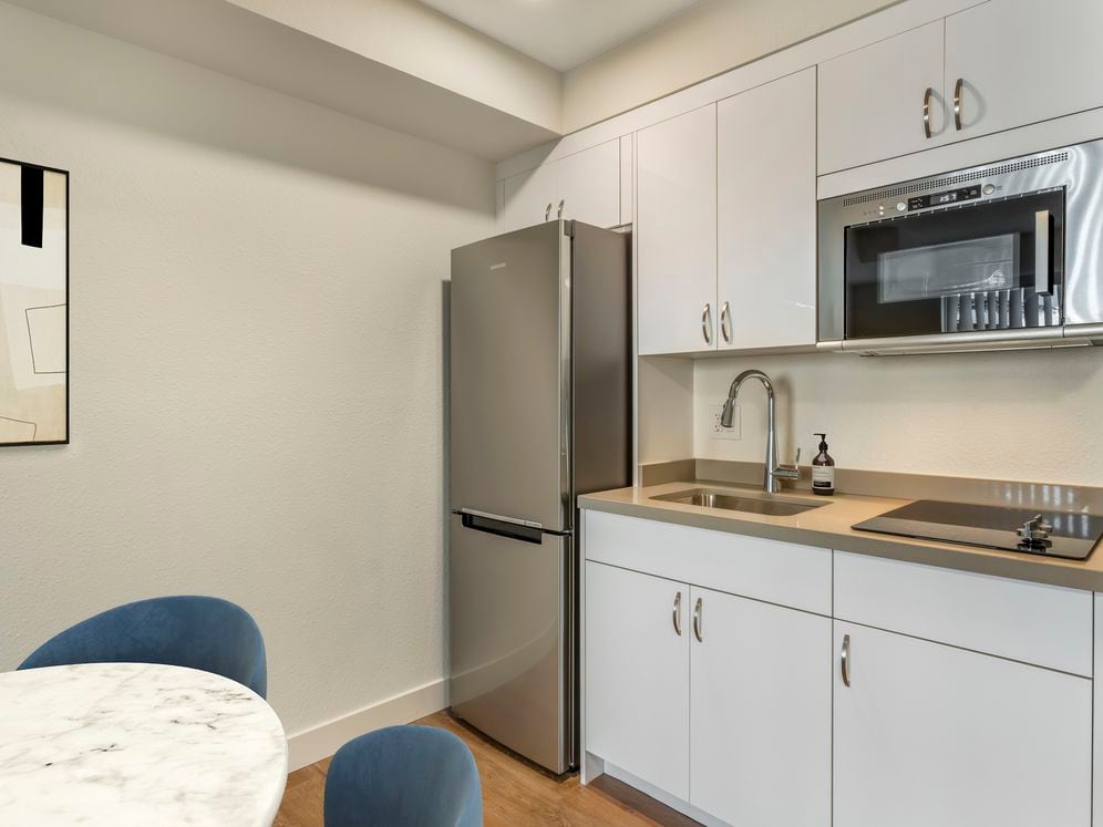 Renovated Package II kitchen with stainless steel appliances, beige quartz countertops, white cabinetry, and hard surface flooring