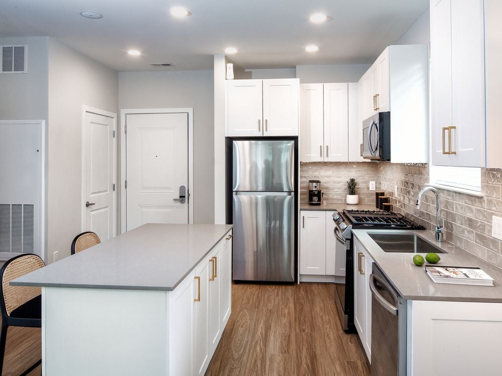 Design Collection II (South Building) Kitchen with white cabinetry, gold pulls, beige tile backsplash, grey quartz countertops, stainless steel appliances, and hard surface flooring
