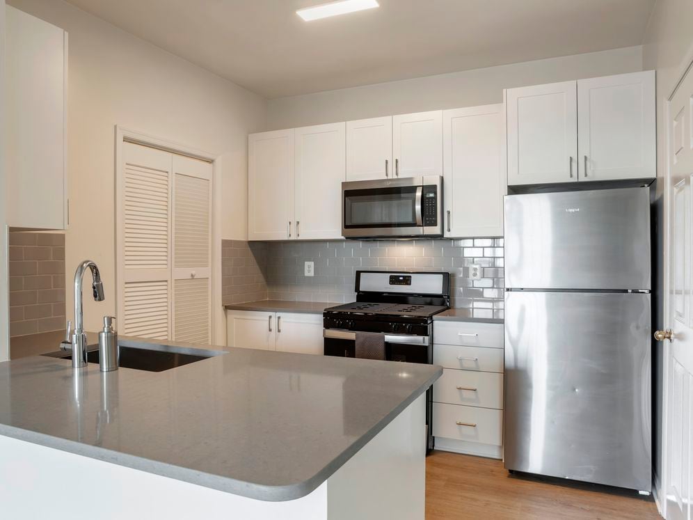 Renovated Package II kitchen with white cabinetry, grey quartz countertops, tile backsplash, stainless steel appliances, and hard surface flooring