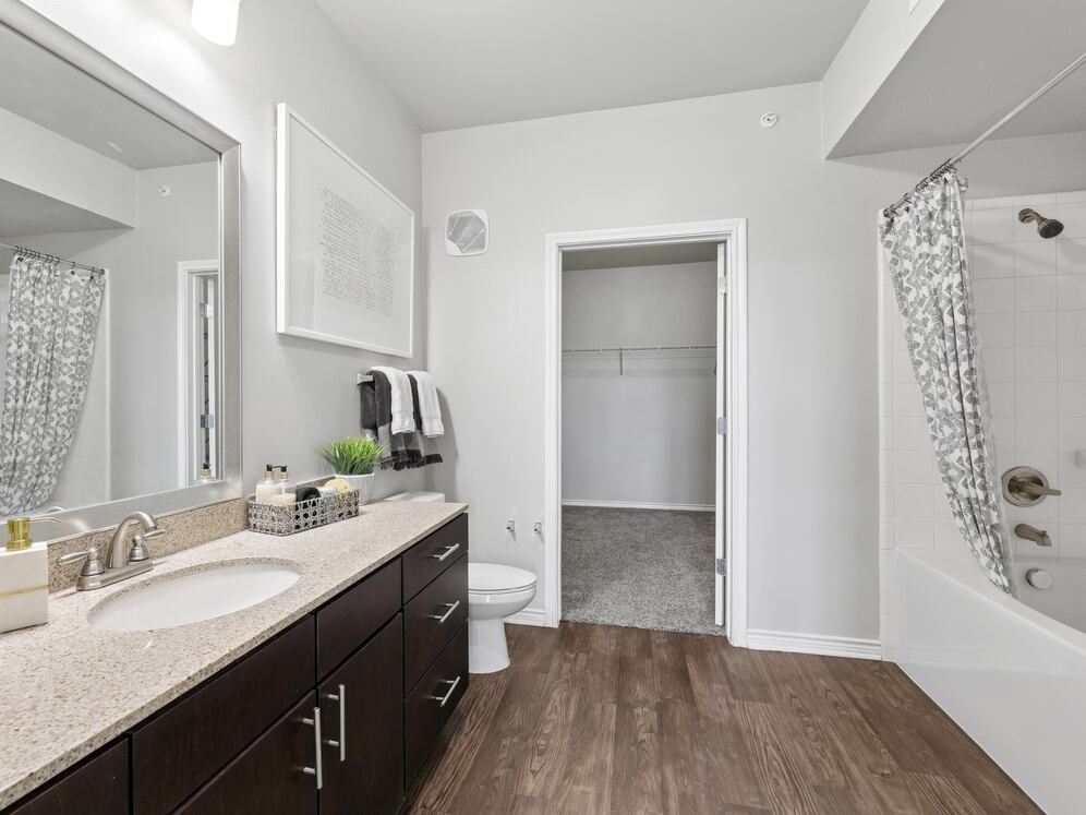 Bath with dark cabinetry, beige speckled granite countertops, and hard surface flooring