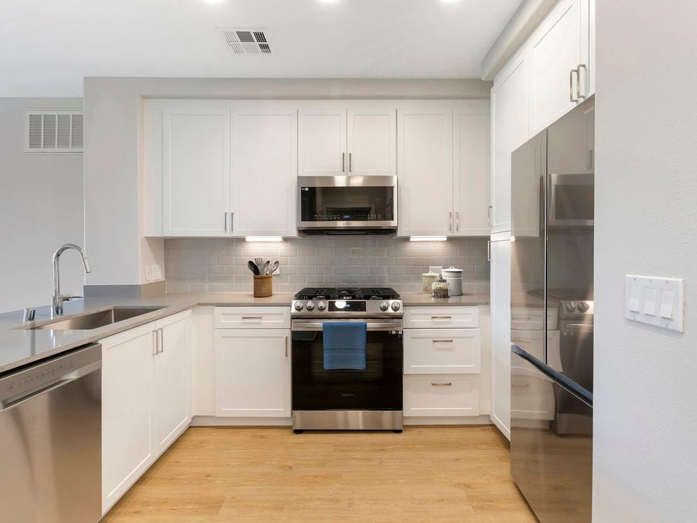 Renovated Package I kitchen with stainless steel appliances, grey quartz countertops, white cabinetry, grey tile backsplash, and hard surface flooring
