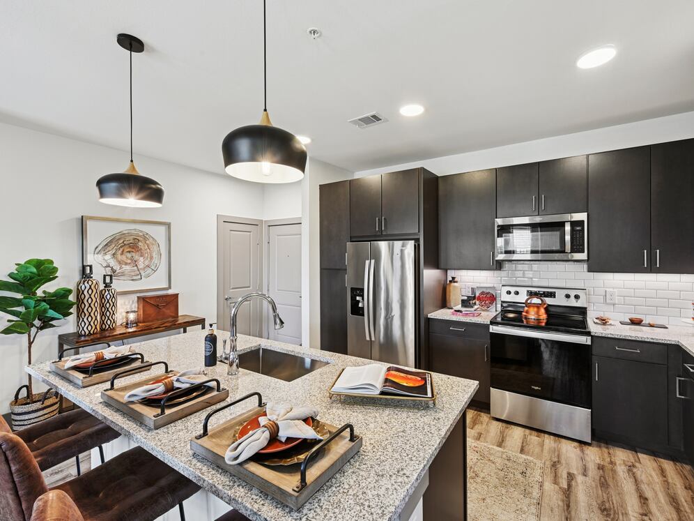 Kitchen with espresso cabinetry, speckled granite countertops, white subway tile backsplash, stainless steel appliances, and hard surface flooring