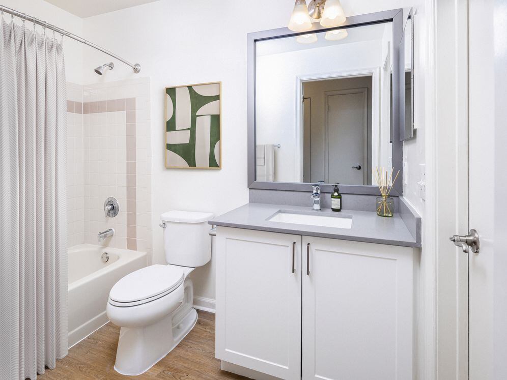 Renovated Package III bath with grey quartz countertops (select homes), white cabinetry, and hard surface flooring
