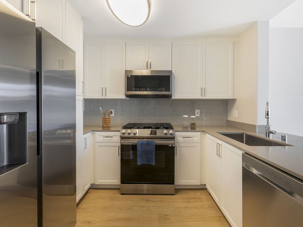 Renovated Package I kitchen with white cabinetry, grey quartz countertops, grey tile backsplash, stainless steel appliances, and hard surface flooring