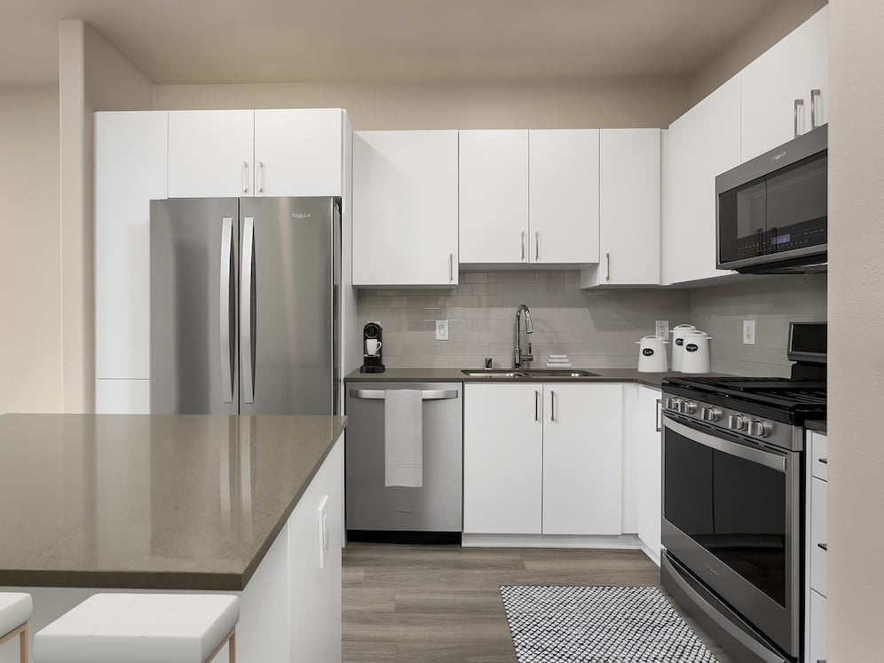 Renovated Package I kitchen with quartz countertops, white cabinetry, stainless steel appliances, hard surface vinyl plank flooring, and tile backsplash