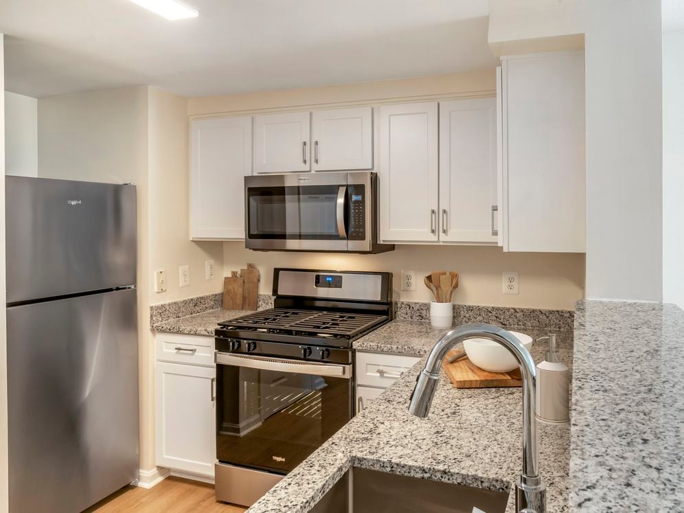 Renovated Package I kitchen with white cabinetry, granite countertops, stainless steel appliances, and hard surface flooring