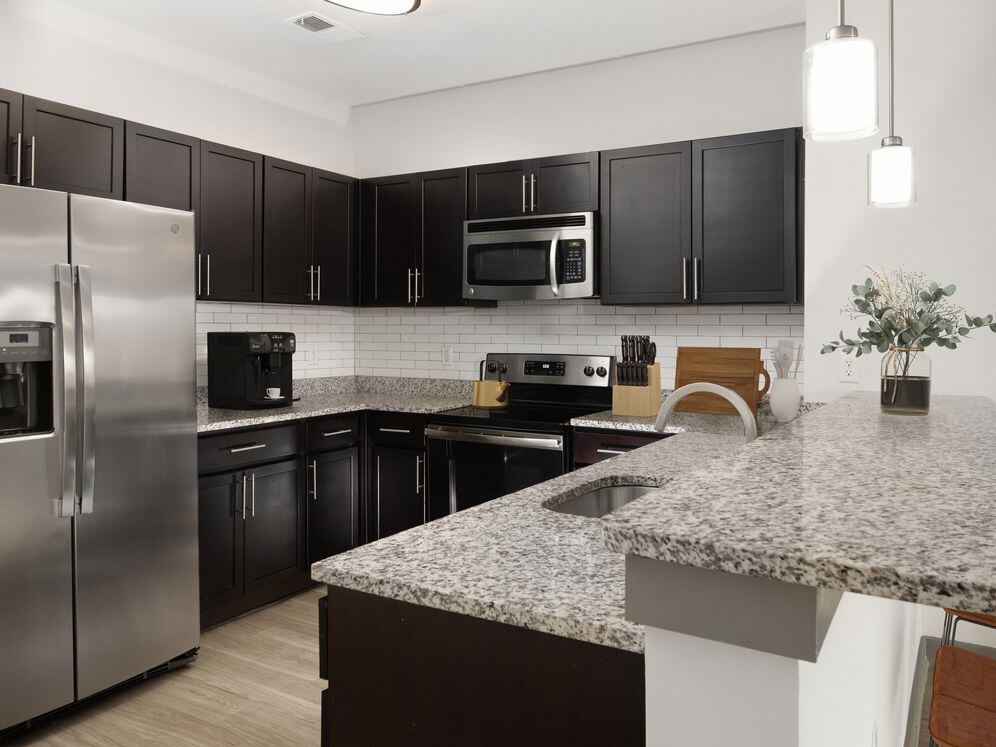 Renovated Package II Kitchen with dark cabinetry, speckled granite countertops, white tile backsplash, stainless steel appliances, pendant lighting, and hard surface flooring