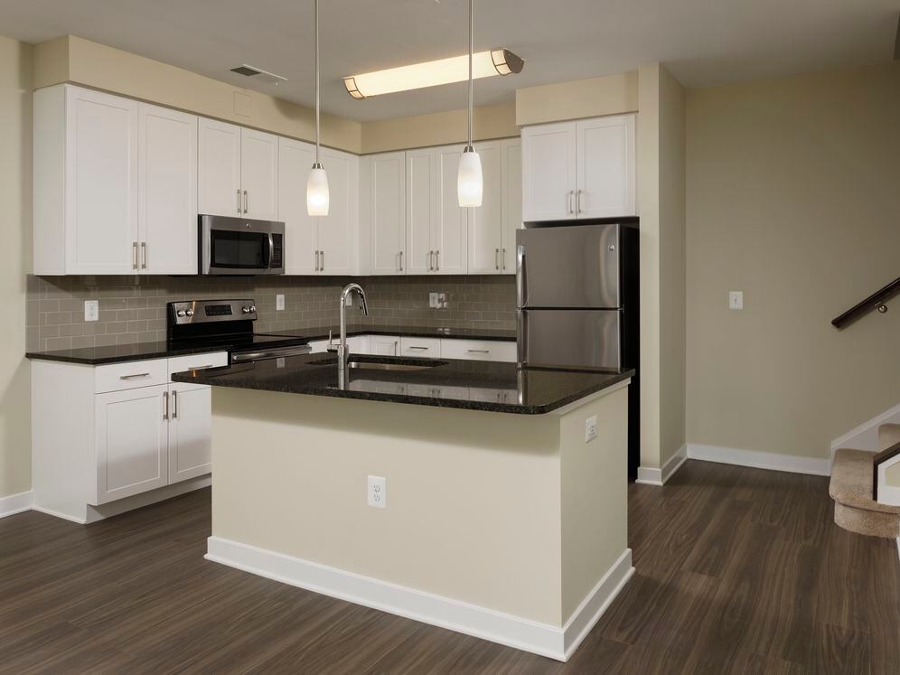 Townhome open concept kitchen with granite countertops and white shaker cabinetry, kitchen island, stainless steel appliances and hard surface flooring