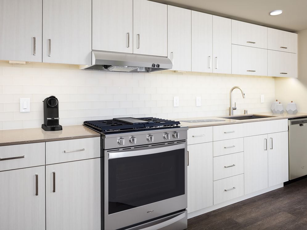 Scheme I kitchen with white cabinetry and undercabinet lighting, quartz countertops, white tile backsplash, stainless steel appliances, and hard surface flooring.