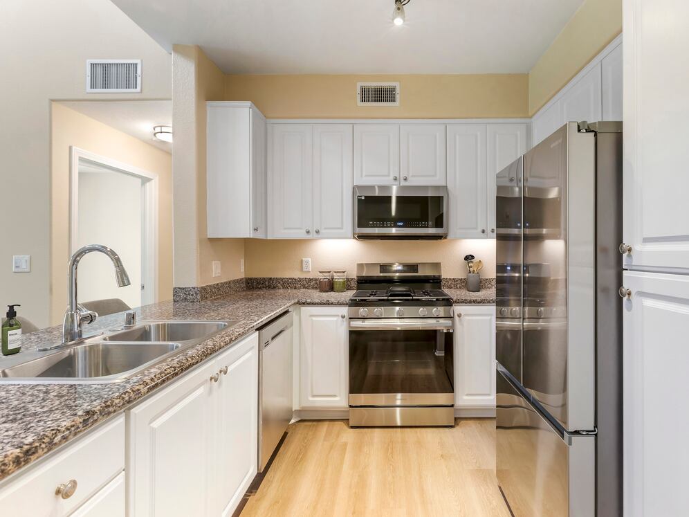 Renovated Package I kitchen with stainless steel appliances, beige speckled granite countertop, white cabinetry, and hard surface flooring