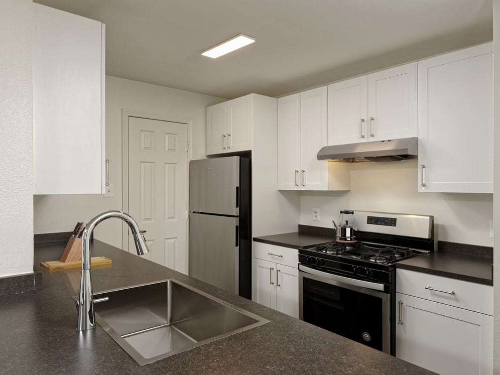 Renovated Package II kitchen with white cabinetry, dark grey laminate countertops, stainless steel appliances, and hard surface flooring