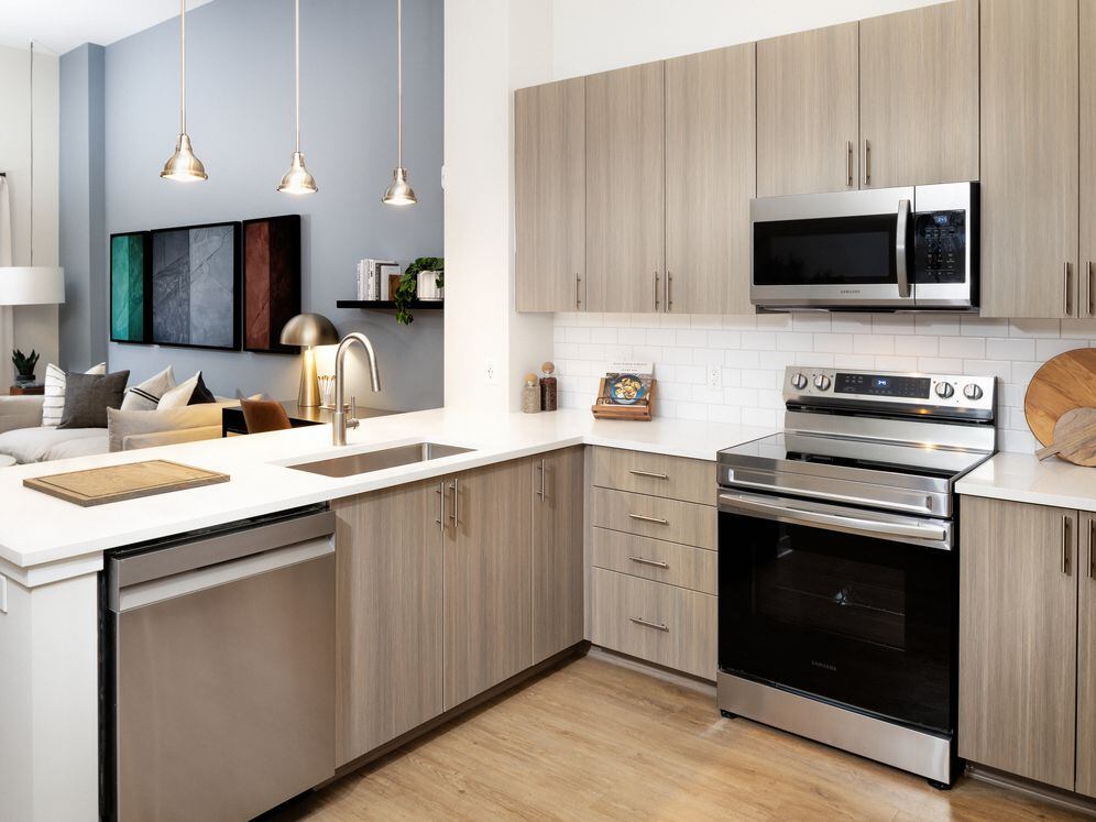 Modern kitchen with oak cabinetry, white tile backsplash, white quartz countertops, stainless steel appliances, and pendant lighting