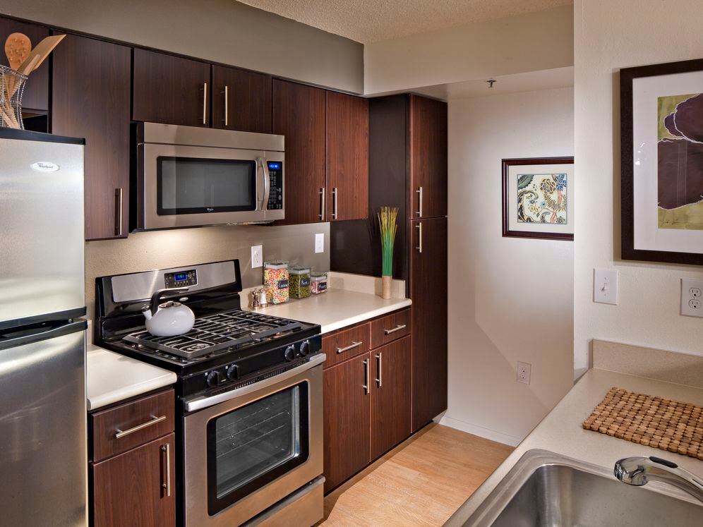 Classic Package I kitchen with espresso cabinetry, beige laminate countertops, stainless steel appliances, and hard surface plank flooring in select units