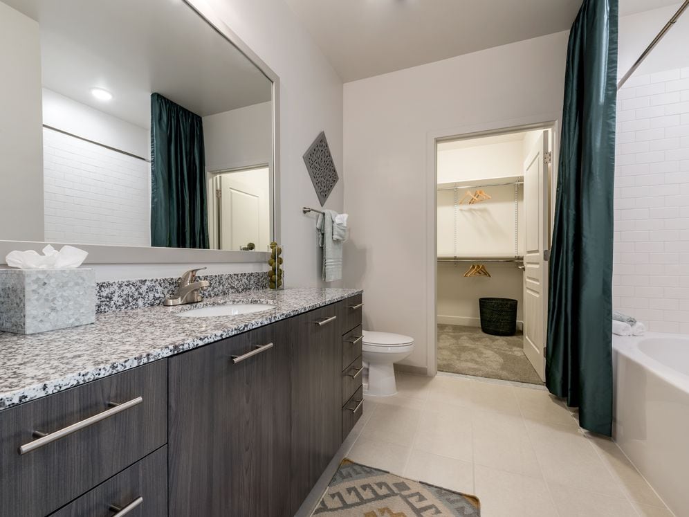 Bath with granite countertops, brown cabinetry, hard surface flooring and walk-in closet