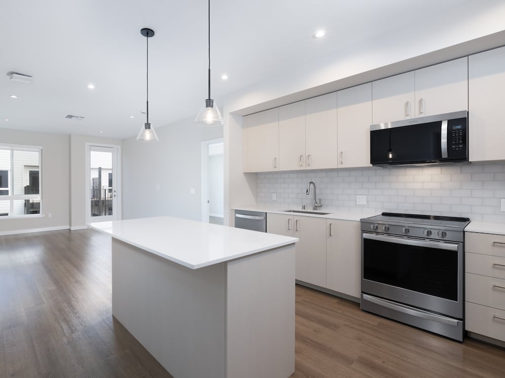 Upgrade Collection Apartment kitchen featuring light cabinetry, white tile backsplash, pendant lighting, white quartz countertops, and hard-surface vinyl plank flooring