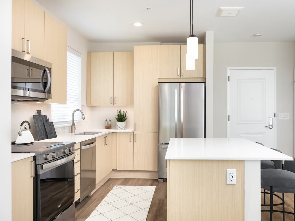 Upgrade Collection I kitchen with stainless steel appliances, white quartz countertops, white tile backsplash, light oak cabinetry, and hard surface flooring