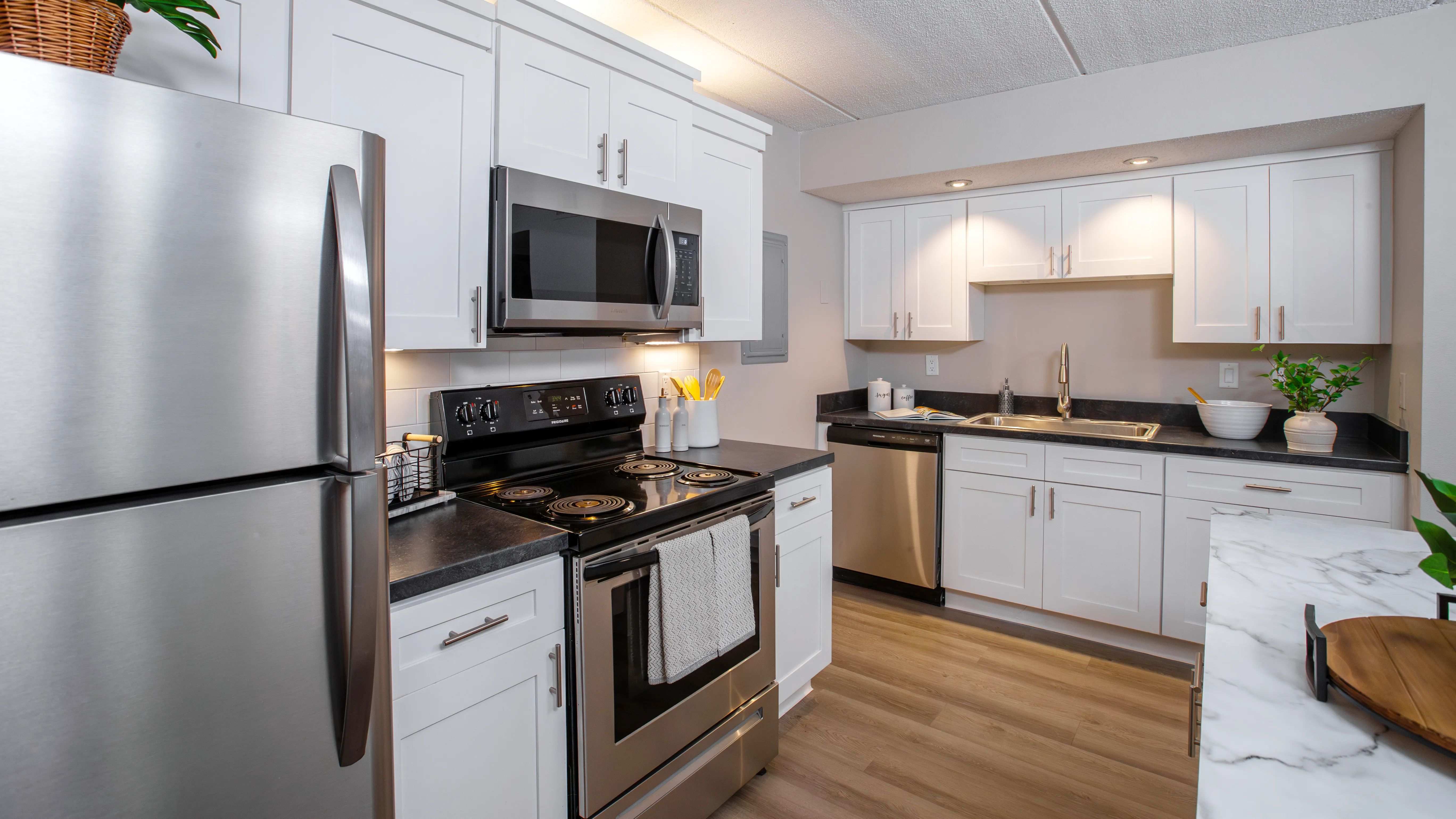 Discover the sleek and functional design of our modern kitchens, featuring stainless steel appliances, black granite-style countertops, and chic white cabinetry, offering the perfect balance of style and efficiency.