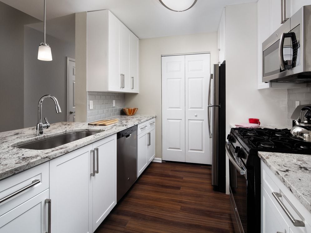 Upgrade Scheme I kitchen with white shaker cabinetry, beige speckled granite countertops, light beige tile backsplash, stainless steel appliances, and hard surface flooring