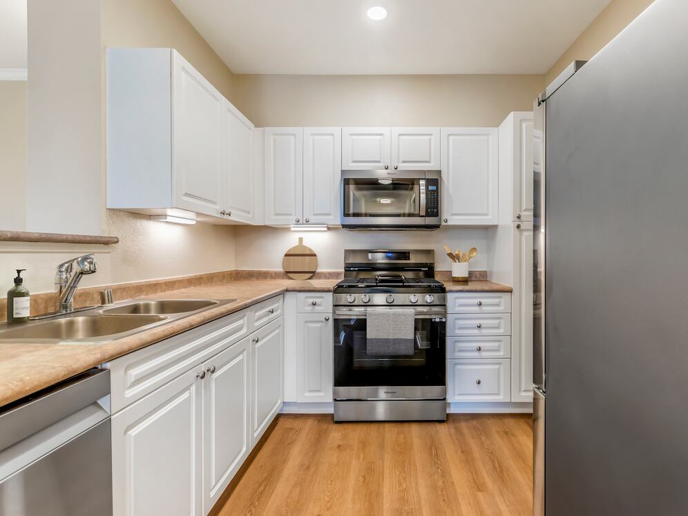 Classic Package II kitchen with upgraded stainless steel appliances, white cabinetry, neutral laminate countertops, and upgraded hard surface flooring