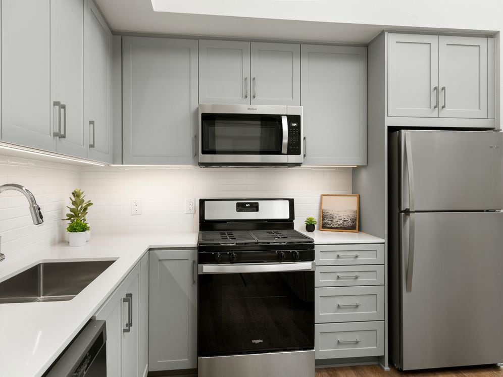 Apartments with modern kitchens featuring grey cabinetry, white quartz stone countertops, white tile backsplash, stainless steel appliances, and hard surface flooring