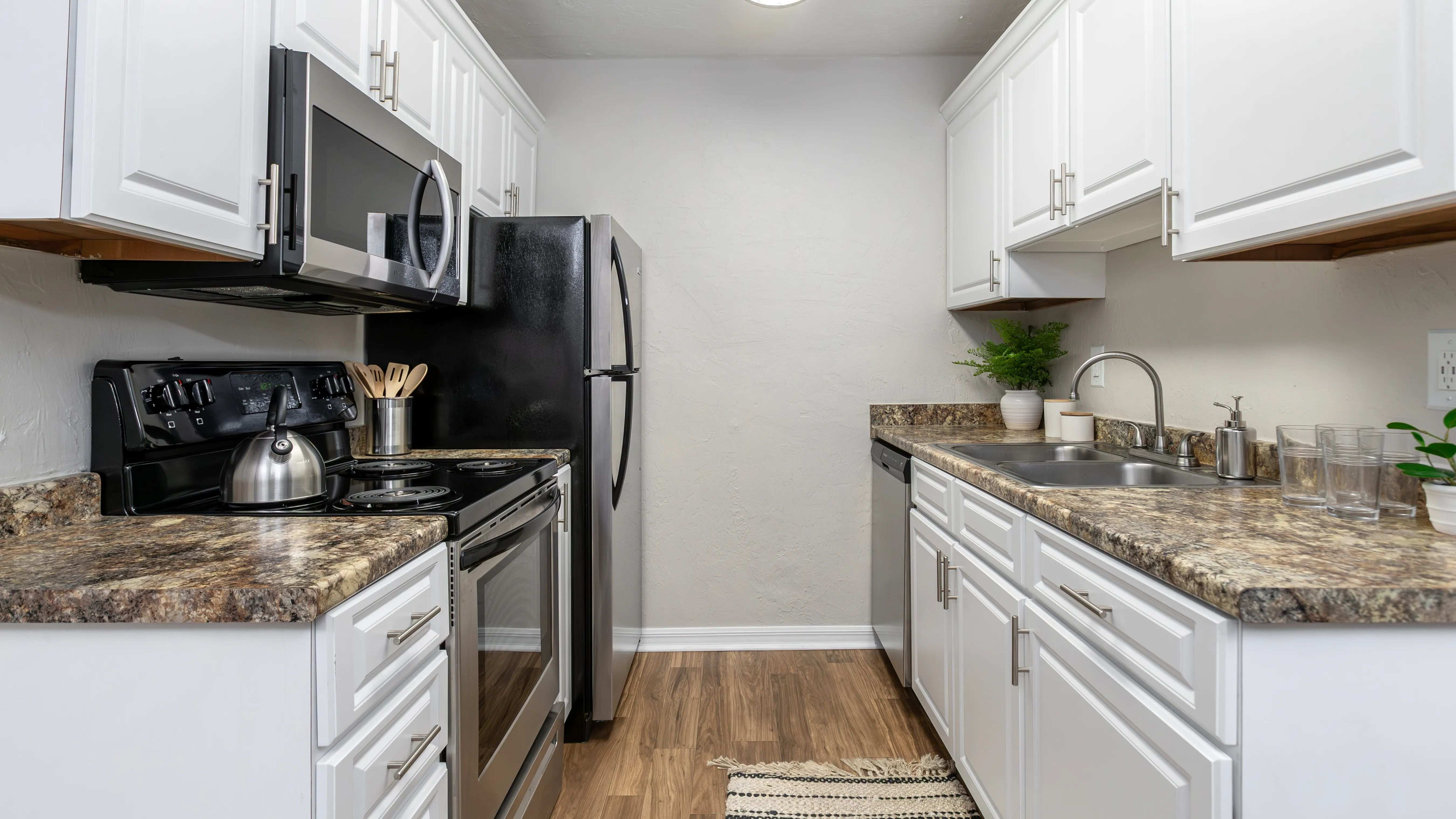 Experience timeless elegance in our updated kitchens, featuring white cabinetry, granite-inspired countertops, and wood-style flooring.