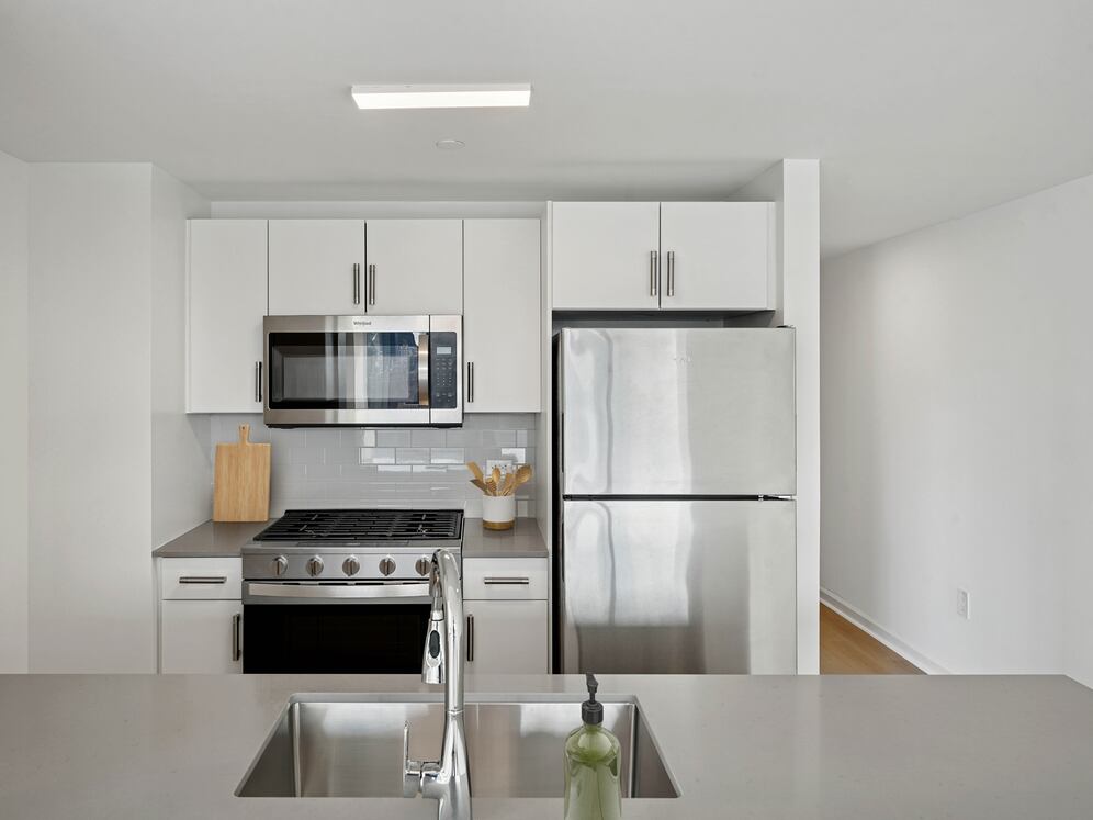 Renovated Package I kitchen with stainless steel appliances, white cabinetry, tile backsplash, grey quartz countertops, and hard-surface flooring