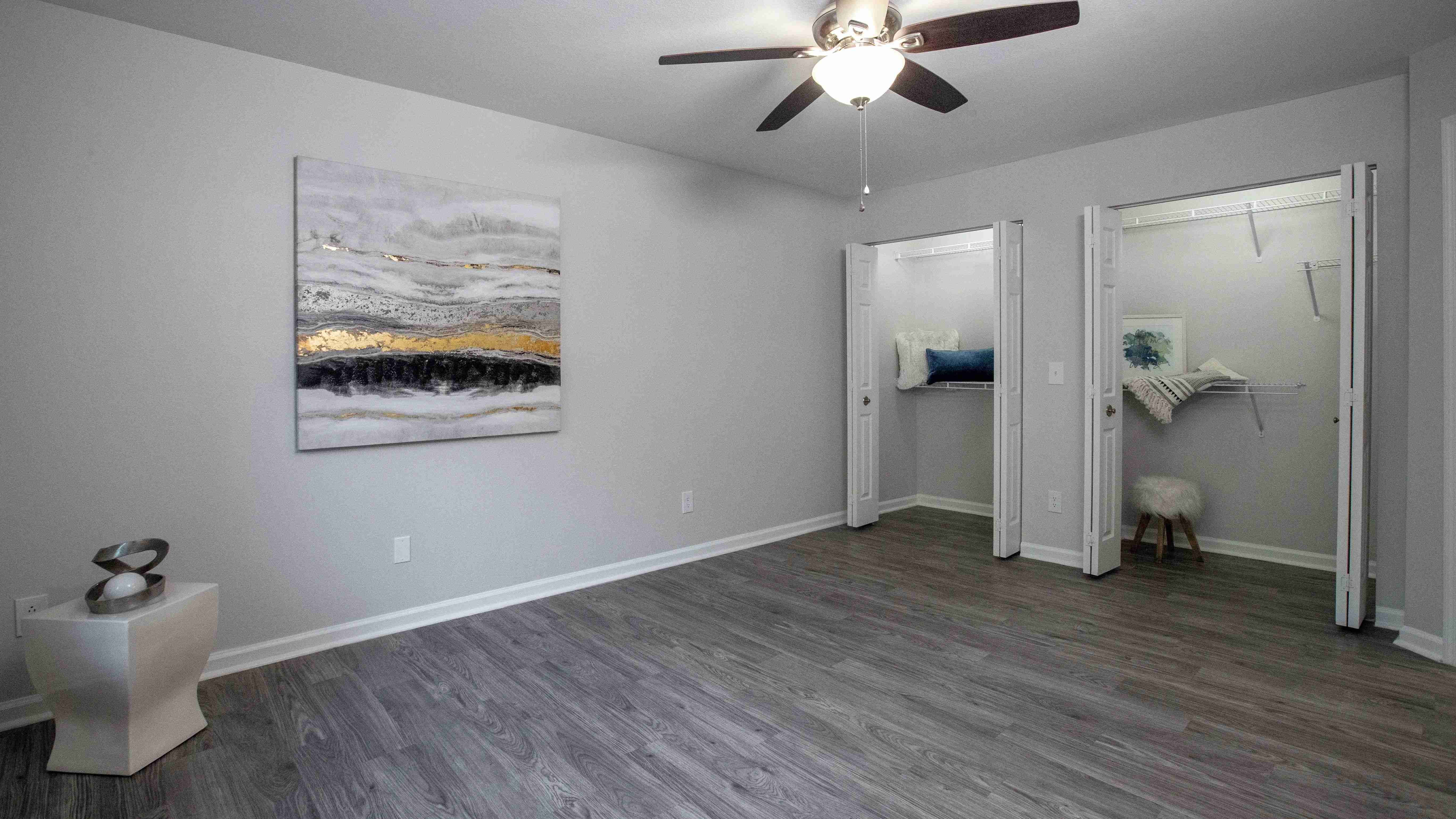 Wood-style flooring, ceiling fan, and generous closet space add a touch of elegance to this spacious bedroom.