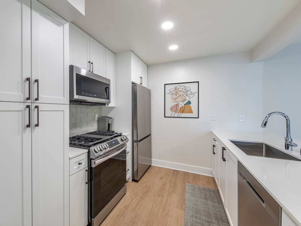 Renovated Package I kitchen with stainless steel appliances, white quartz countertops, white cabinetry, light grey tile backsplash, and hard surface flooring