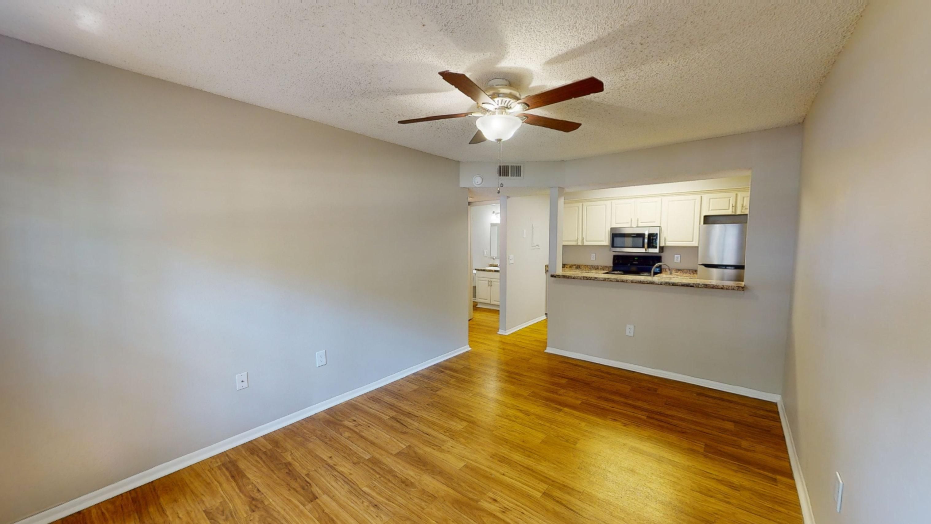 The Oakwood floor plan offers a bright and welcoming living area featuring wood-style flooring, a ceiling fan, and an open layout that flows seamlessly into the kitchen.