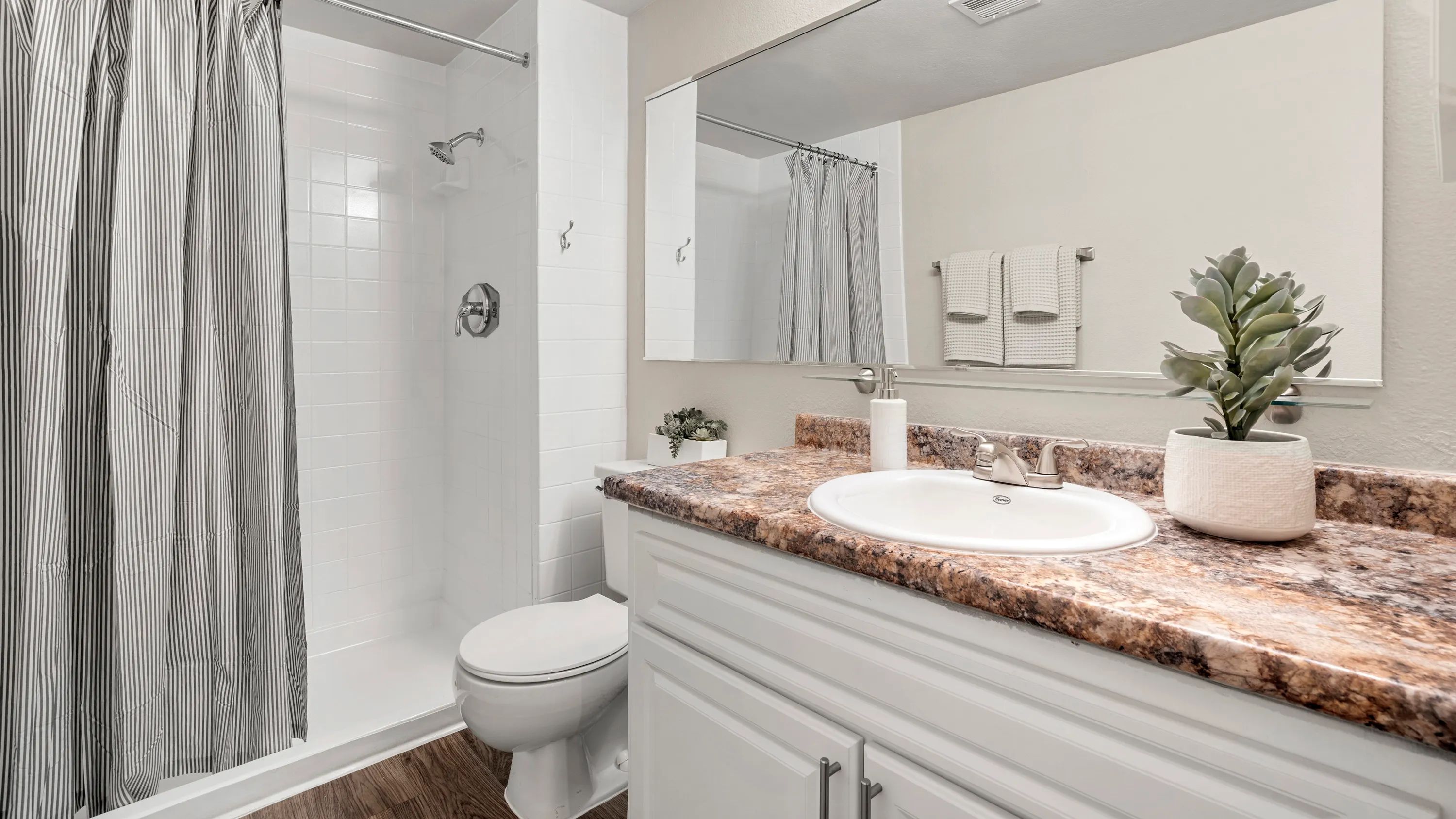 Revel in the luxurious master bathroom oasis, featuring wood-style flooring, an oversized vanity, and a generously sized mirror, ensuring ultimate comfort and style.