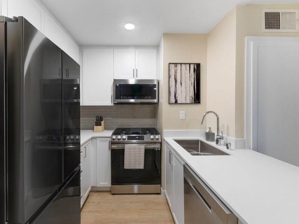 Renovated Package I kitchen with stainless steel appliances, white quartz countertops, white cabinetry, grey tile backsplash, and hard surface flooring
