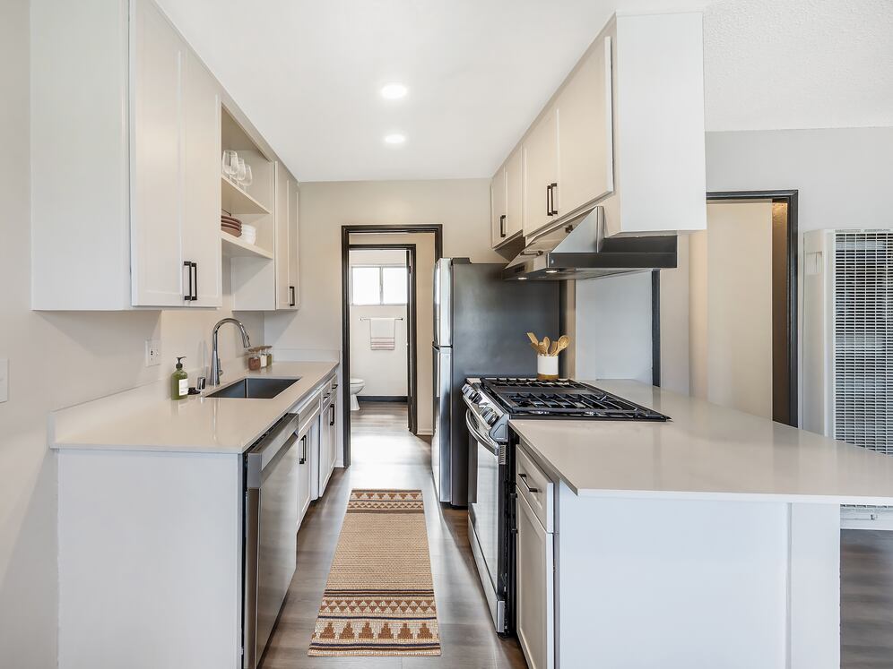 Renovated Package I kitchen with stainless steel appliances, white quartz countertops, white cabinetry, and hard surface flooring (select homes)