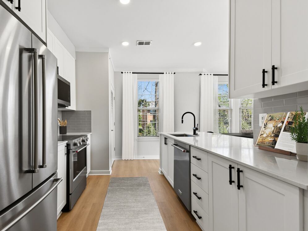 Renovated Package II kitchen with stainless steel appliances, white cabinetry, grey tile backsplash, white quartz countertops, and hard surface flooring