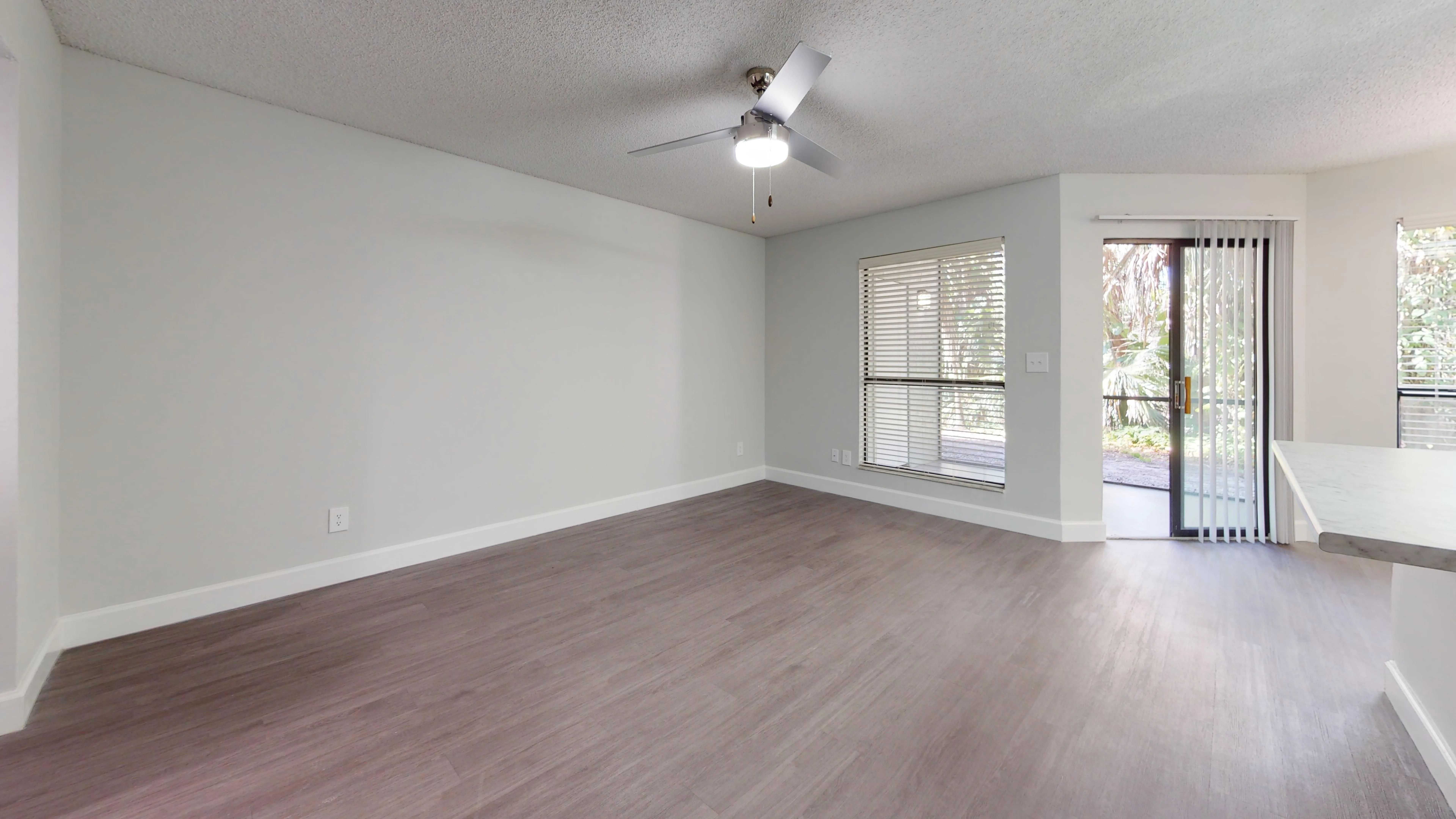 The Martinique floor plan offers a spacious living room filled with natural light, featuring modern flooring, a ceiling fan, and direct access to a private patio through sliding glass doors.