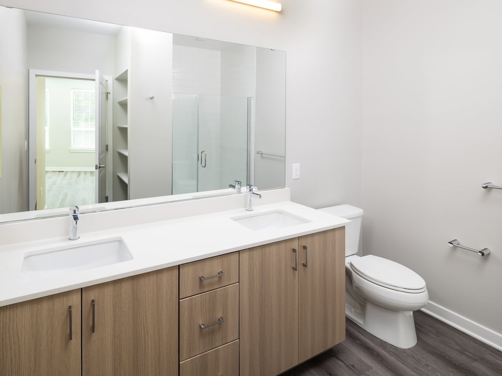 New West Phase - Finish Package IV Bathroom with double sink, white quartz countertops, oak cabinetry, and hard surface flooring