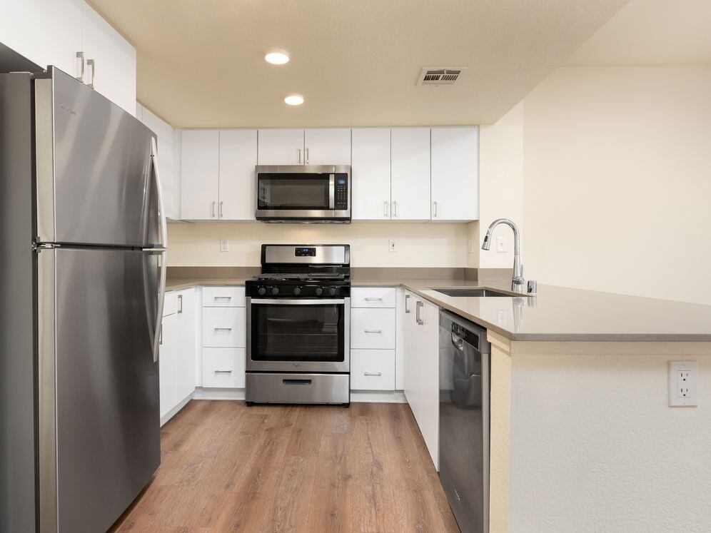 Renovated Package I kitchen with stainless steel appliances, grey quartz countertops, white flat cabinetry, and hard surface flooring