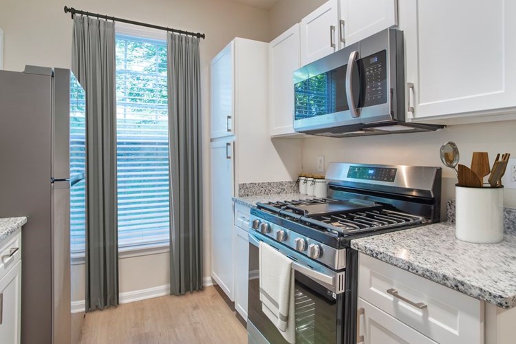 Renovated Package II kitchen with stainless steel appliances, white speckled quartz countertops, white cabinetry, and hard surface flooring