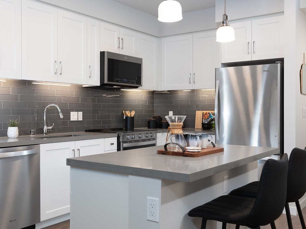 Upgrade Collection kitchen with stainless steel appliances, white cabinetry, grey quartz countertop, grey tile backsplash, and hard surface flooring