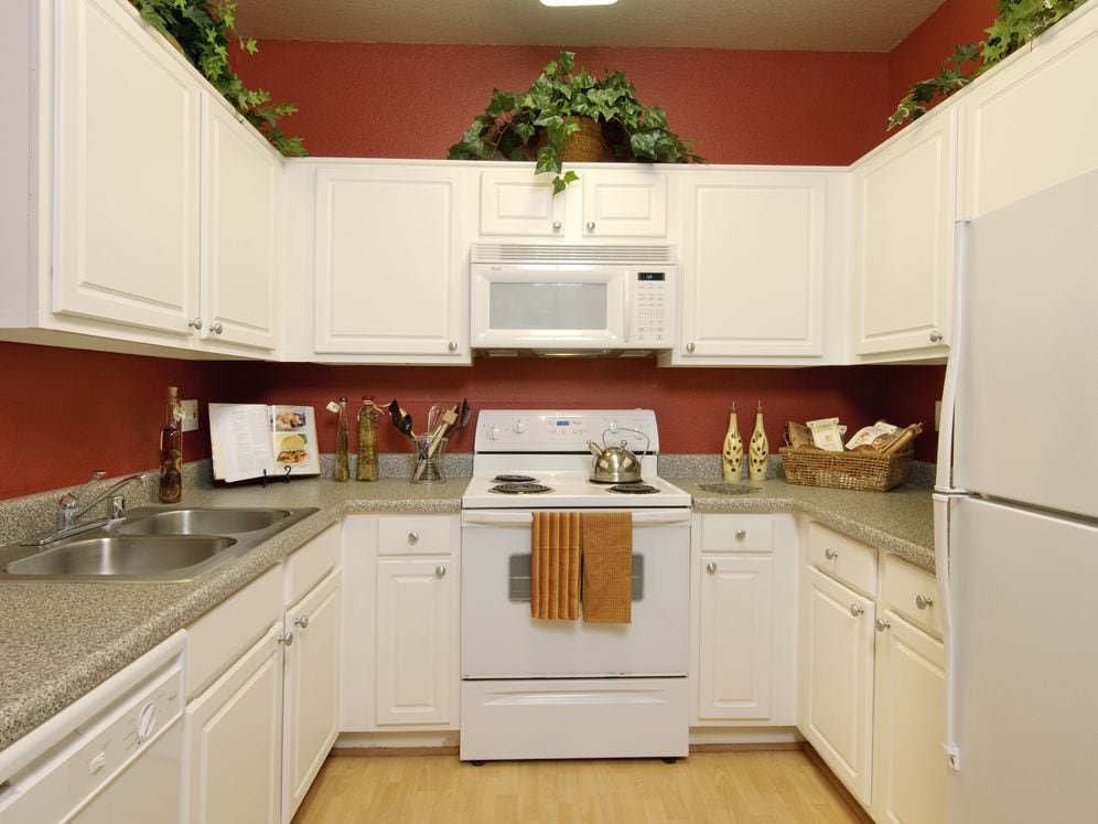 Kitchens with white appliances, grey speckled laminate countertops, and white cabinetry