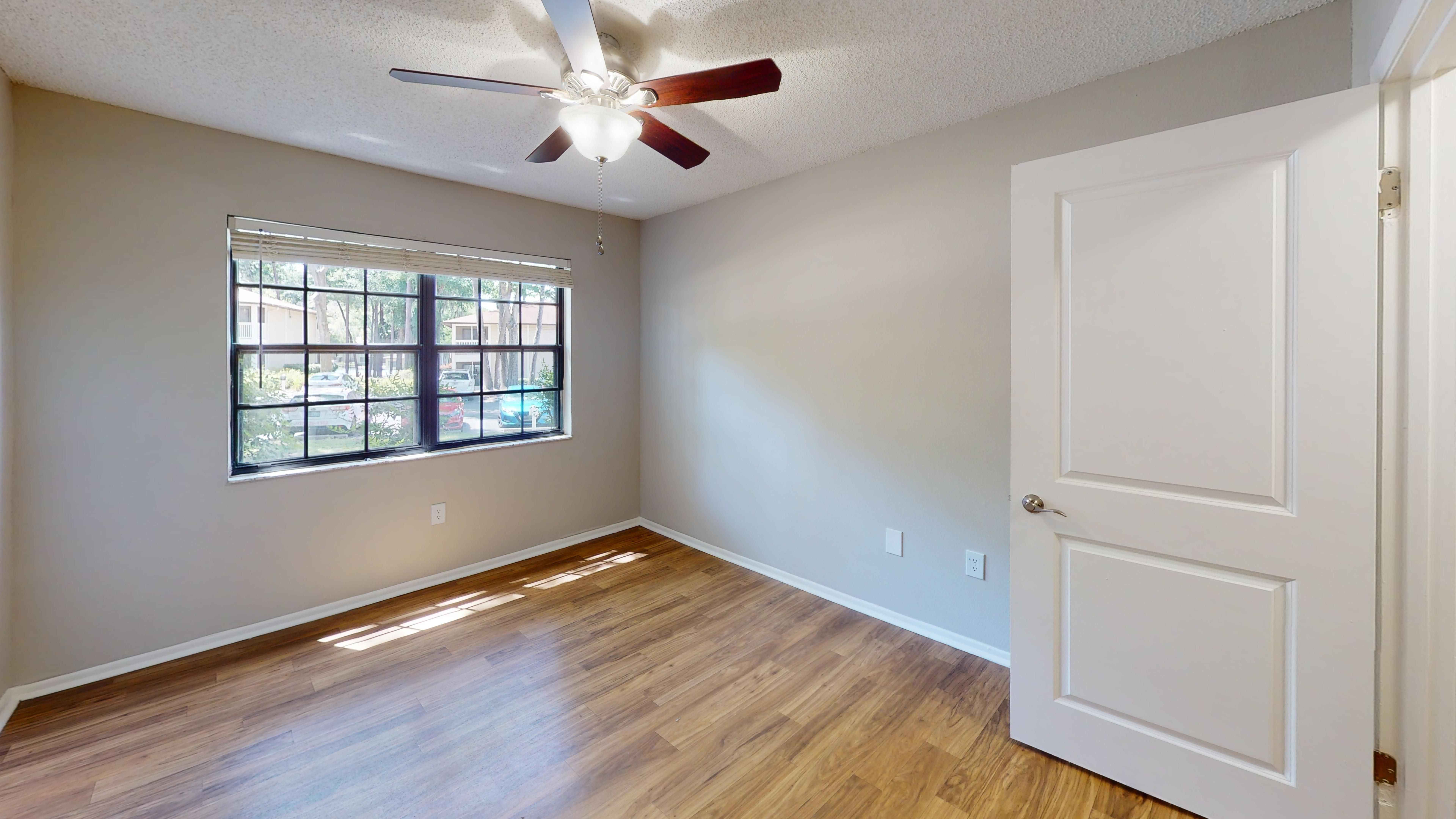The bedroom in The Oakwood floor plan features wood-style flooring, a ceiling fan, and abundant natural light from the large windows. This inviting space offers the perfect setting to relax, recharge, and make yourself at home.