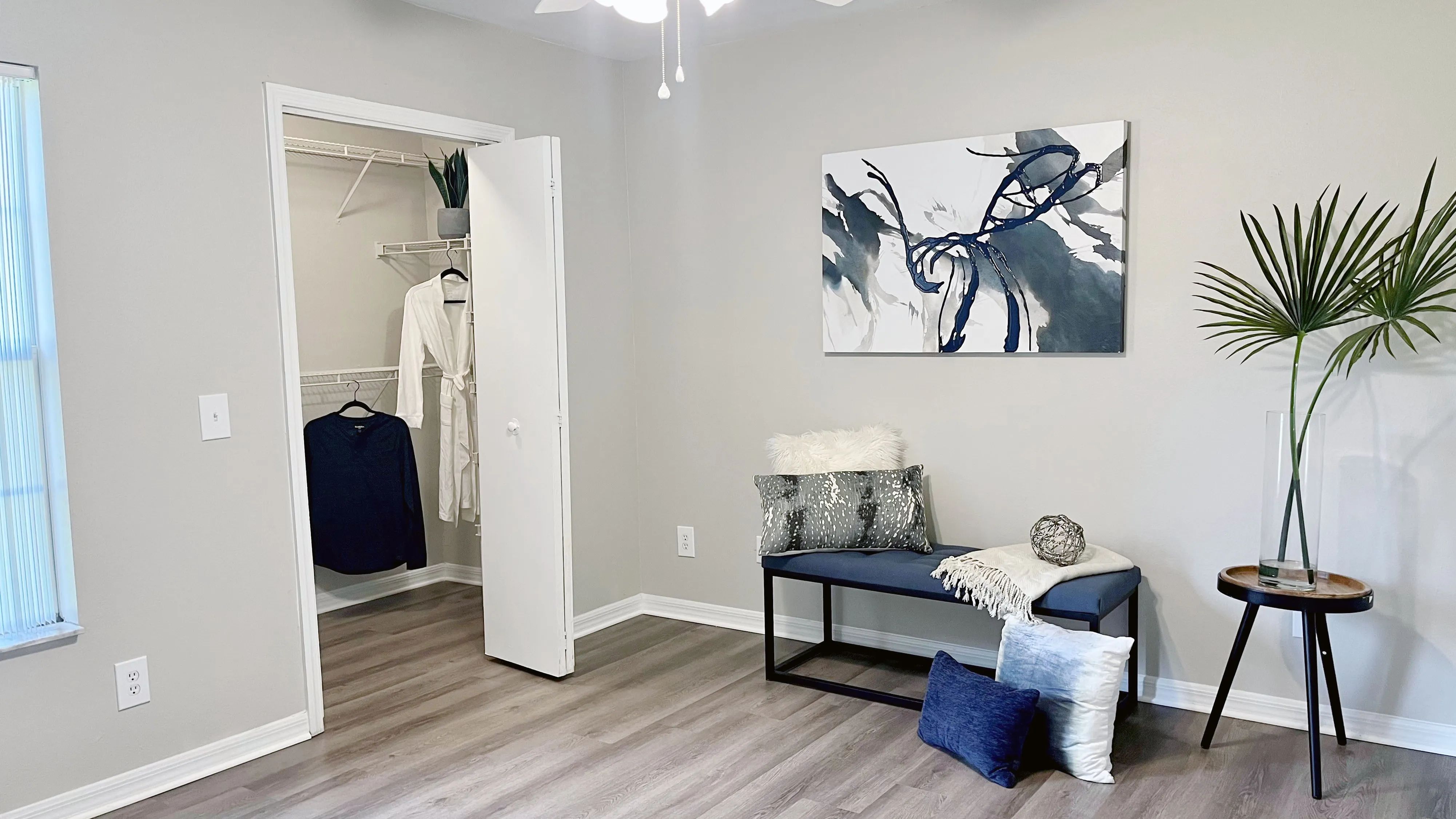 Experience the epitome of comfort in our signature master bedroom at Eagle's Pointe featuring sleek wood-style flooring, a spacious walk-in closet, and a convenient lighted ceiling fan.
