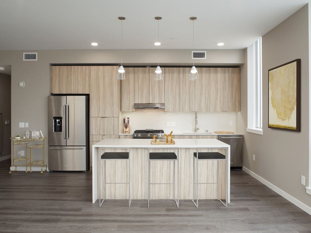 Signature Collection penthouse kitchen with oak cabinetry and undercabinet lighting, white quartz countertops and backsplash, upgraded stainless steel appliances, and hard surface flooring.