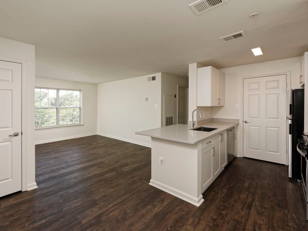 Renovated Package II kitchen and living areas with light grey quartz countertops, white cabinetry, stainless steel appliances, and hard surface flooring