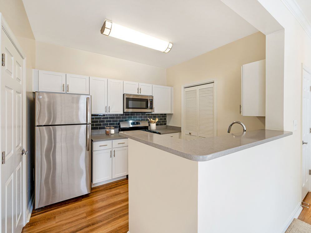 Renovated Package I kitchen with white cabinetry, grey quartz countertops, dark grey subway tile backsplash, stainless steel appliances, and hard surface flooring